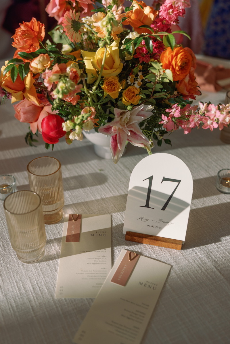 Table with a floral centerpiece, two clear glasses, two printed menus, and a white table number card displaying the number 17 and a date.