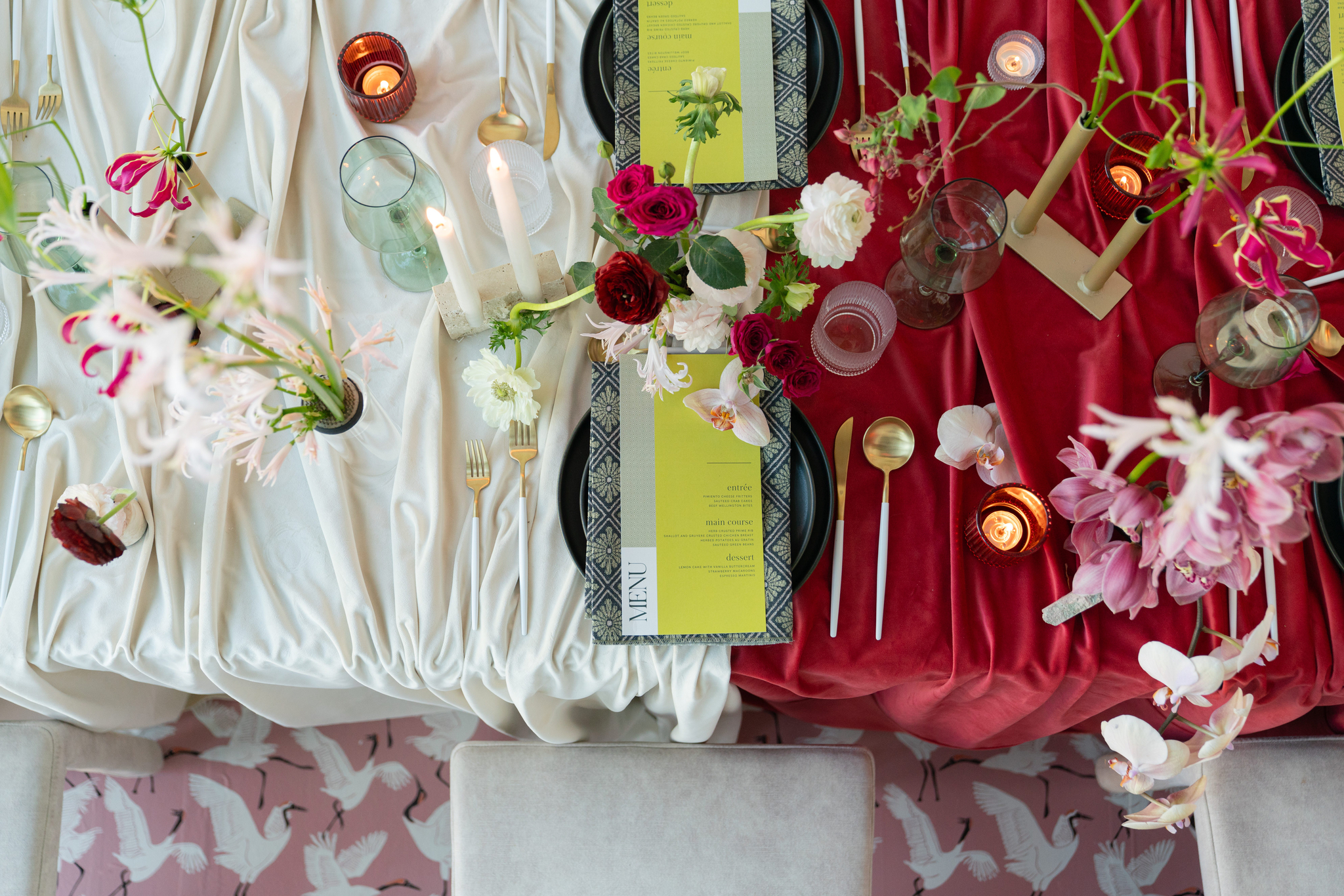 Overhead view of an elegant table setting with red and white tablecloths, floral arrangements, candles, gold cutlery, and two place settings with menus.