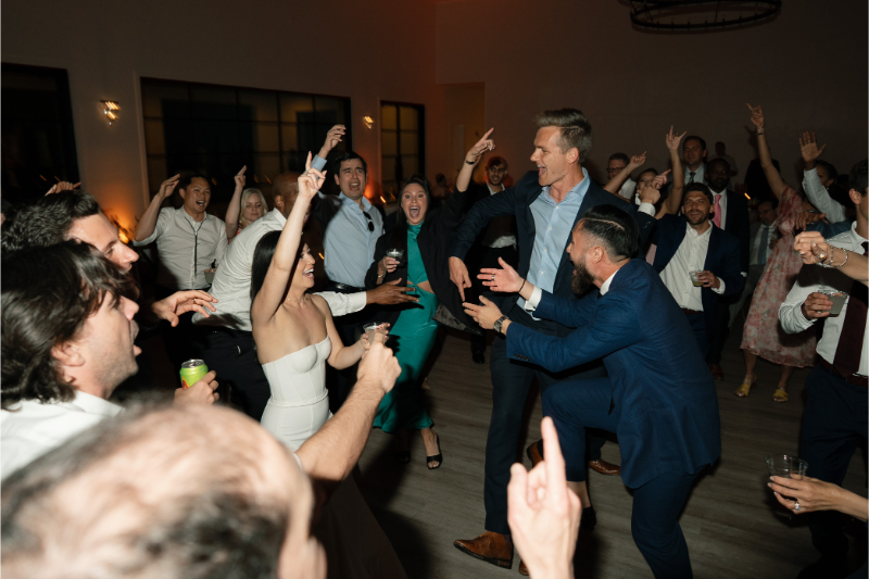 A group of people in formal attire dance energetically at The Arlo Austin, with several individuals raising their hands and smiling.
