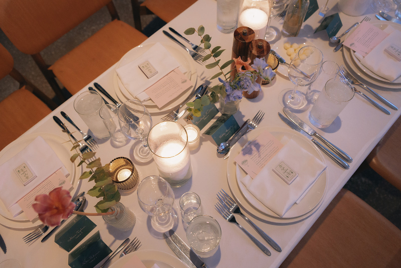 Wedding design ideas from a formal table setting with plates, utensils, glasses, candles, small floral arrangements, and name cards on a white tablecloth.