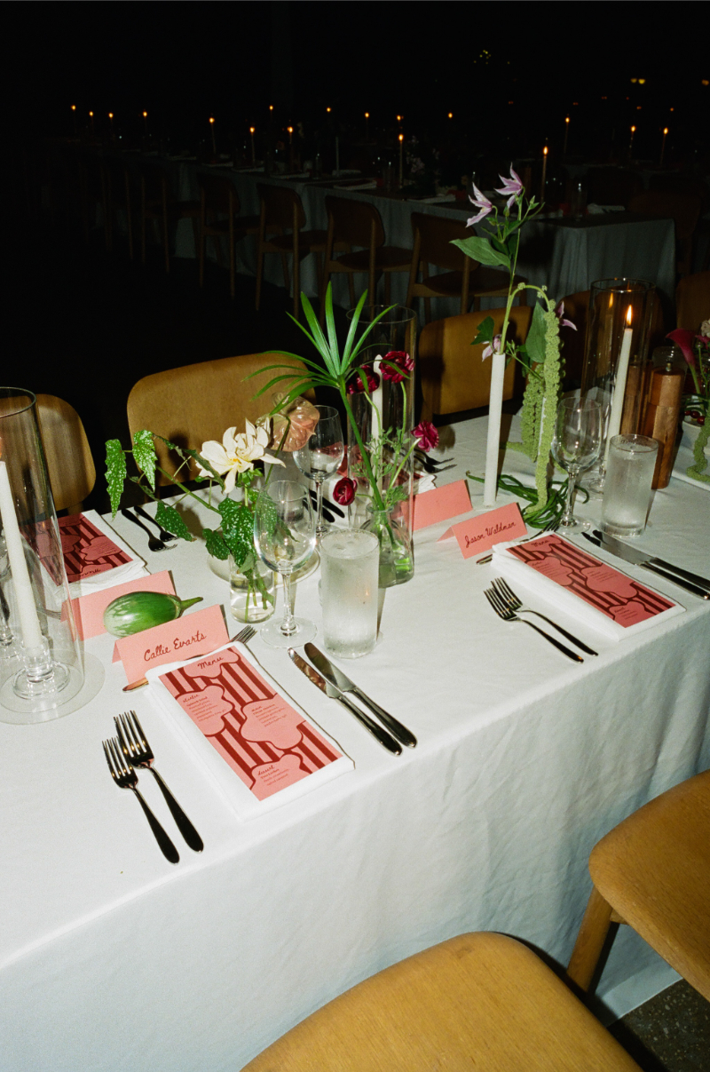 A long dining table set with pink menus, name cards, glassware, cutlery, candles, and assorted floral centerpieces—perfect inspiration for your wedding budget checklist.