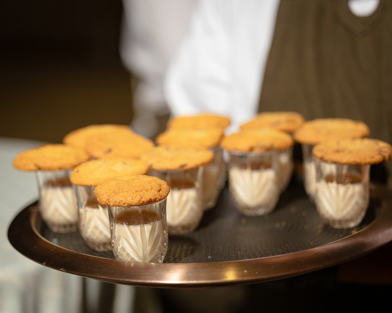 A tray with small glasses of milk, each topped with a chocolate chip cookie.