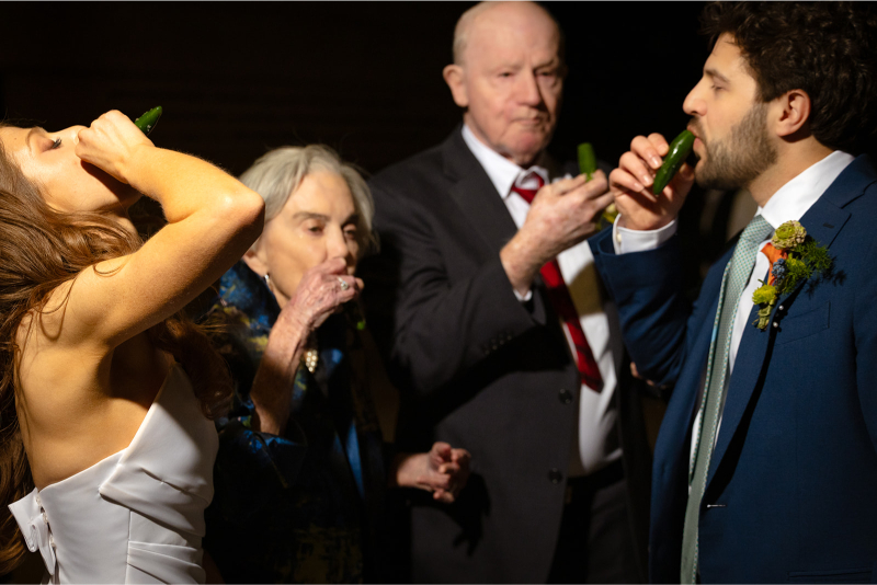 Four people, dressed formally, drink from jalapeno shoots at a wedding reception. The lighting is focused on the group.