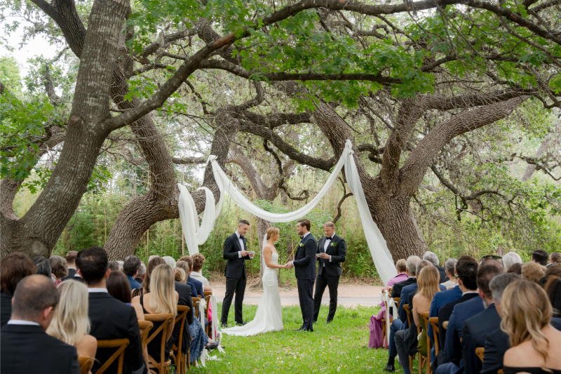 Outdoor wedding ceremony at Mattie's Austin wedding venue under large trees with draped white fabric
